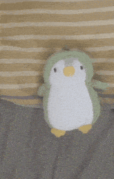 a stuffed penguin wearing a green hat is sitting on a bed