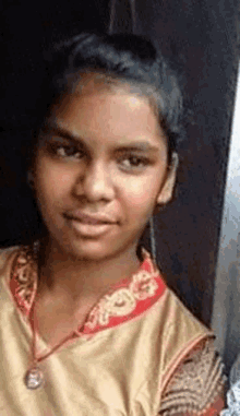 a young girl wearing a gold shirt and a red collar is looking at the camera and smiling .