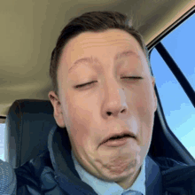 a man in a suit and tie is making a funny face while sitting in a car .