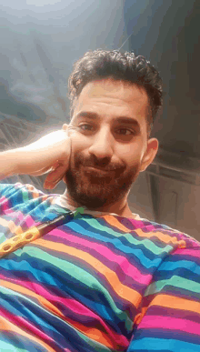 a man with a beard wearing a colorful striped shirt looks at the camera