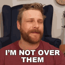 a man with a beard is sitting in a chair and says " i 'm not over them "