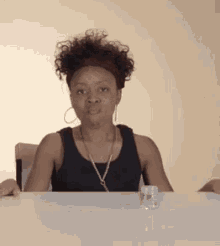 a woman with curly hair is sitting at a table with a bottle of water in front of her .