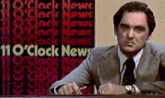 a man in a suit and tie sits in front of a 110 o clock news sign