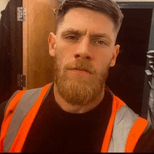 a man with a beard is wearing a safety vest and taking a selfie .