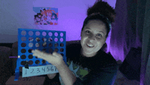 a woman is holding a connect four board with the numbers 1234567 on it