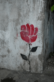 a red fist shaped rose is painted on a concrete wall