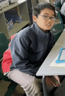 a young boy wearing glasses sits at a desk with a tablet in front of him