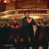 a man in a suit is dancing in front of a group of men with sony music written in the corner