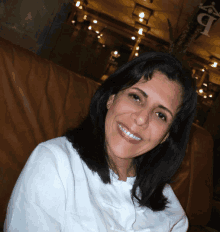 a woman in a white shirt smiles while sitting on a brown leather chair