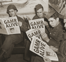 a group of soldiers are reading a newspaper which says gamr alive