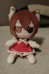 a stuffed animal with a cat ear and a red dress is sitting on a bed