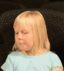 a little girl is sitting in a chair with her eyes closed and making a funny face .