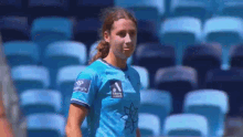 a woman in a blue shirt is standing in front of a row of blue seats in a stadium .