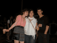 a man and two women pose for a picture while one woman is holding a cup of beer