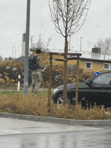 a man with a backpack is standing next to a black car in a parking lot