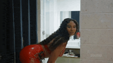 a woman in a red dress is standing next to a brick wall that says zeus