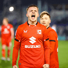 a man wearing a red suzuki jersey shouts