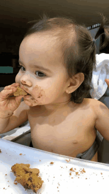 a little girl is eating a cookie with a messy face