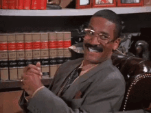 a man in a suit and tie is smiling while sitting in a chair in front of a shelf of books .