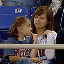 a woman and a little girl are sitting in a stadium watching a baseball game with the number 12 on the seat