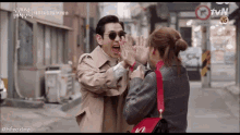 a man and a woman are standing next to each other on a street with a tvn sign in the background