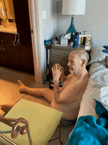 a naked man sits on the floor in front of a nightstand with a water bottle that says adidas on it