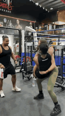 a man in a black tank top is holding a woman in a gym with a sign on the wall that says ' mma '