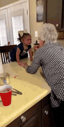 a little girl is sitting at a kitchen counter with an older woman and a sign that says " rules of the kitchen "