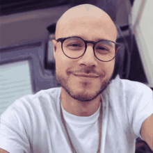 a bald man with glasses and a beard wears a white shirt