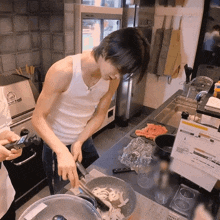 a man in a white tank top is cooking in a kitchen with a sign on the counter that says ' cooking ' on it