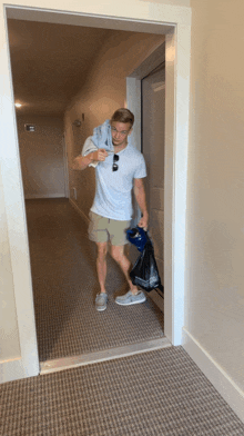 a man in a white shirt and khaki shorts is walking down a hallway carrying a blue bag