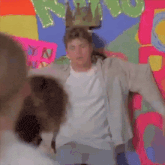 a man with a crown on his head is standing in front of a colorful wall with people .