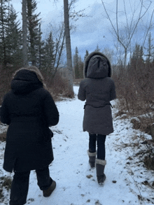 two women are walking down a snowy path with trees in the background