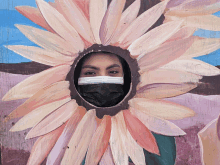 a woman wearing a mask looks through a hole in a flower painting