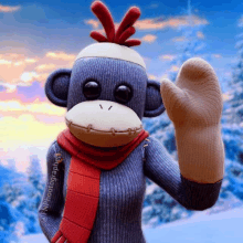 a sock monkey wearing a scarf and hat is waving at the camera