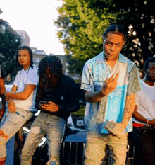 a group of young men are standing in front of a car and one man is giving the middle finger