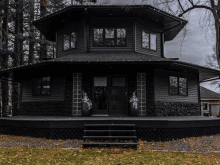 a black house with a black roof and a black porch surrounded by trees .