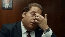 a man in a suit and tie is rubbing his forehead .