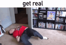 a man in a red shirt is laying on the floor in front of a bookshelf with the words get real above him