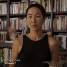 a woman in a black tank top is standing in front of a bookshelf with the words prime video on the bottom