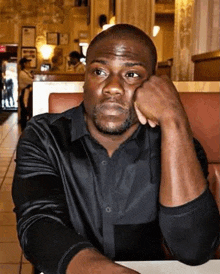 a man in a black shirt is sitting at a table in a restaurant with his head resting on his hand .