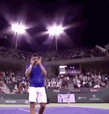 a man in a blue shirt and white shorts is standing on a tennis court in front of a crowd .