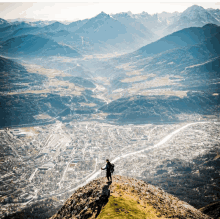 a person standing on top of a mountain looking down at a city below