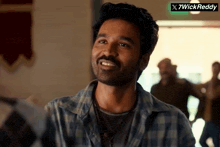 a man in a plaid shirt smiles in front of a sign that says x7wickreddy