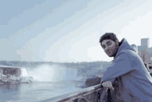 a man leaning on a railing looking at the waterfall