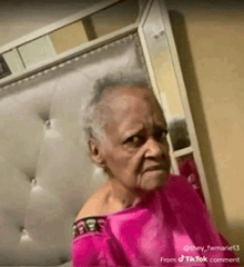 an elderly woman in a pink shirt is sitting in front of a mirror .