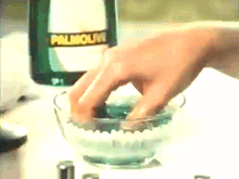 a bottle of palmolive sits on a counter next to a hand