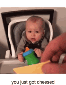 a baby is sitting in a high chair with a bottle and a piece of cheese in front of him .