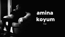 a black and white photo of a man sitting in a chair with the words amina koyum behind him