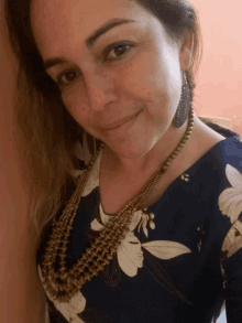 a woman wearing a floral shirt and a necklace smiles for the camera